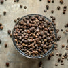 Whole ground pepper corns filling the glass bowl and scattered on the table. 