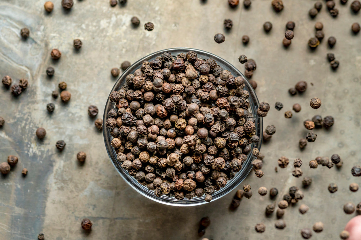 Whole ground pepper corns filling the glass bowl and scattered on the table. 